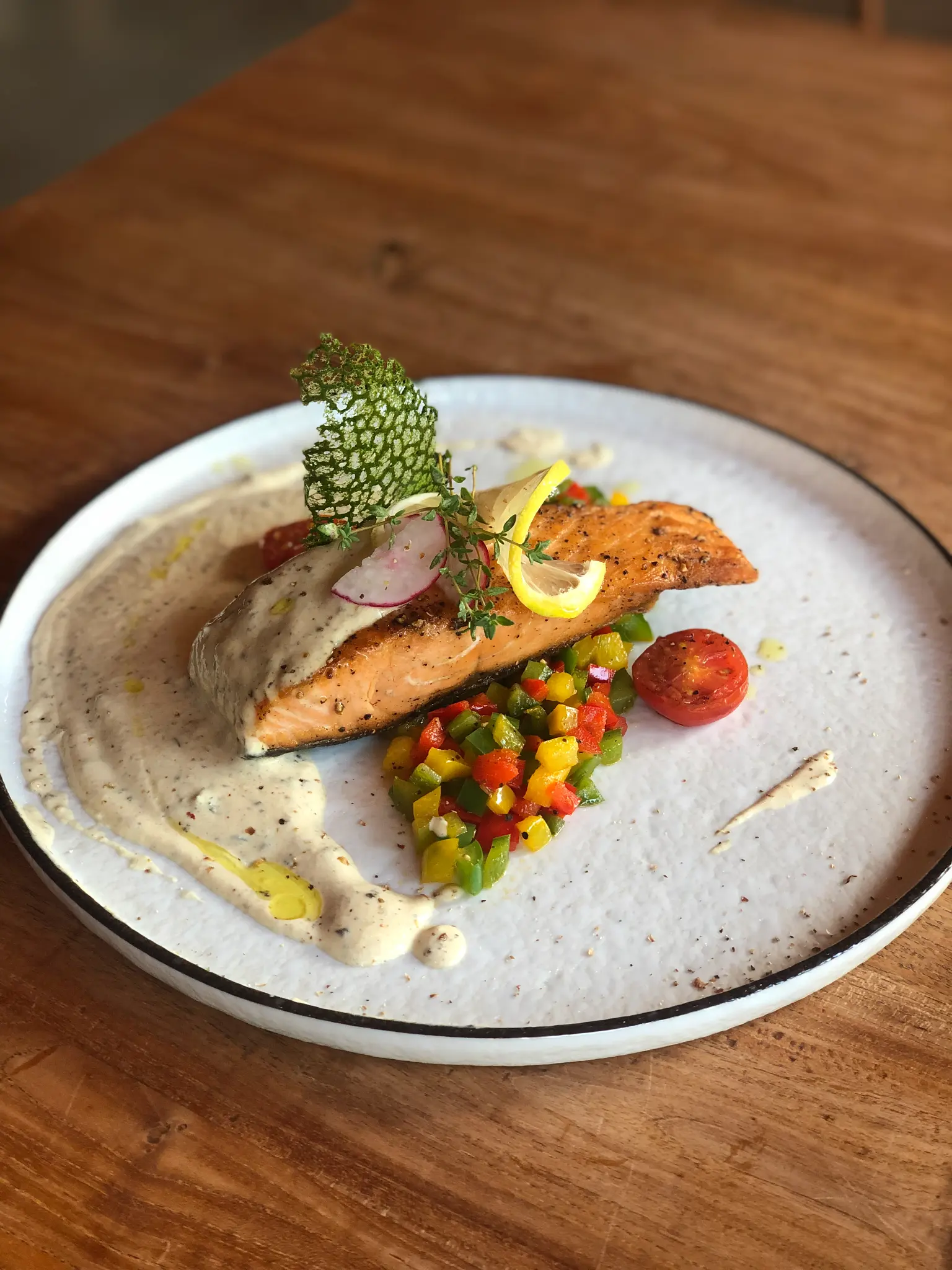 Fish with garden vegetables. A seared fish fillet is plated with colourful vegetables, fresh greens and a light sauce.