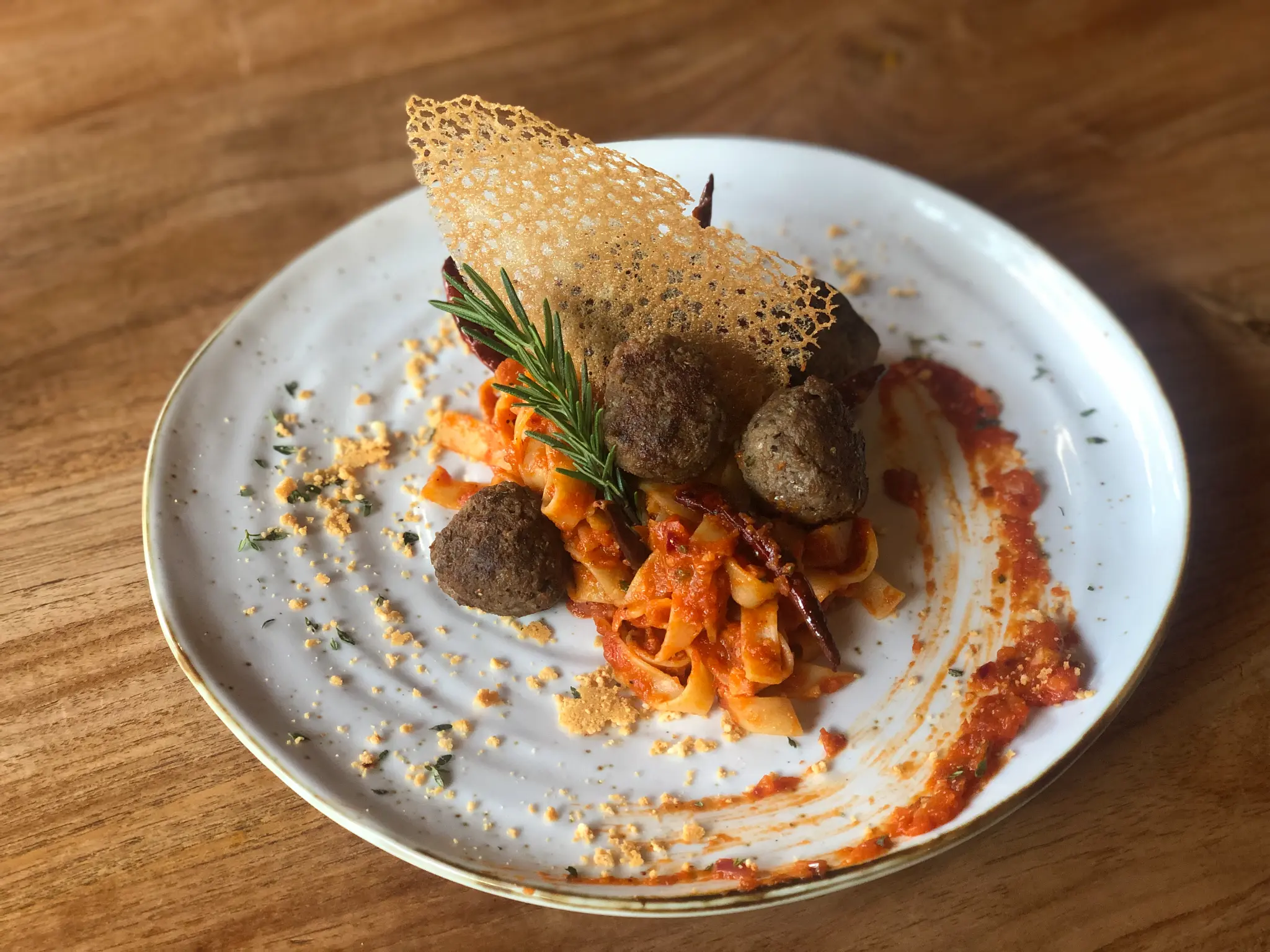 Pasta with a crisp garnish. A warm pasta dish is presented on a white plate with herbs and a golden crisp.