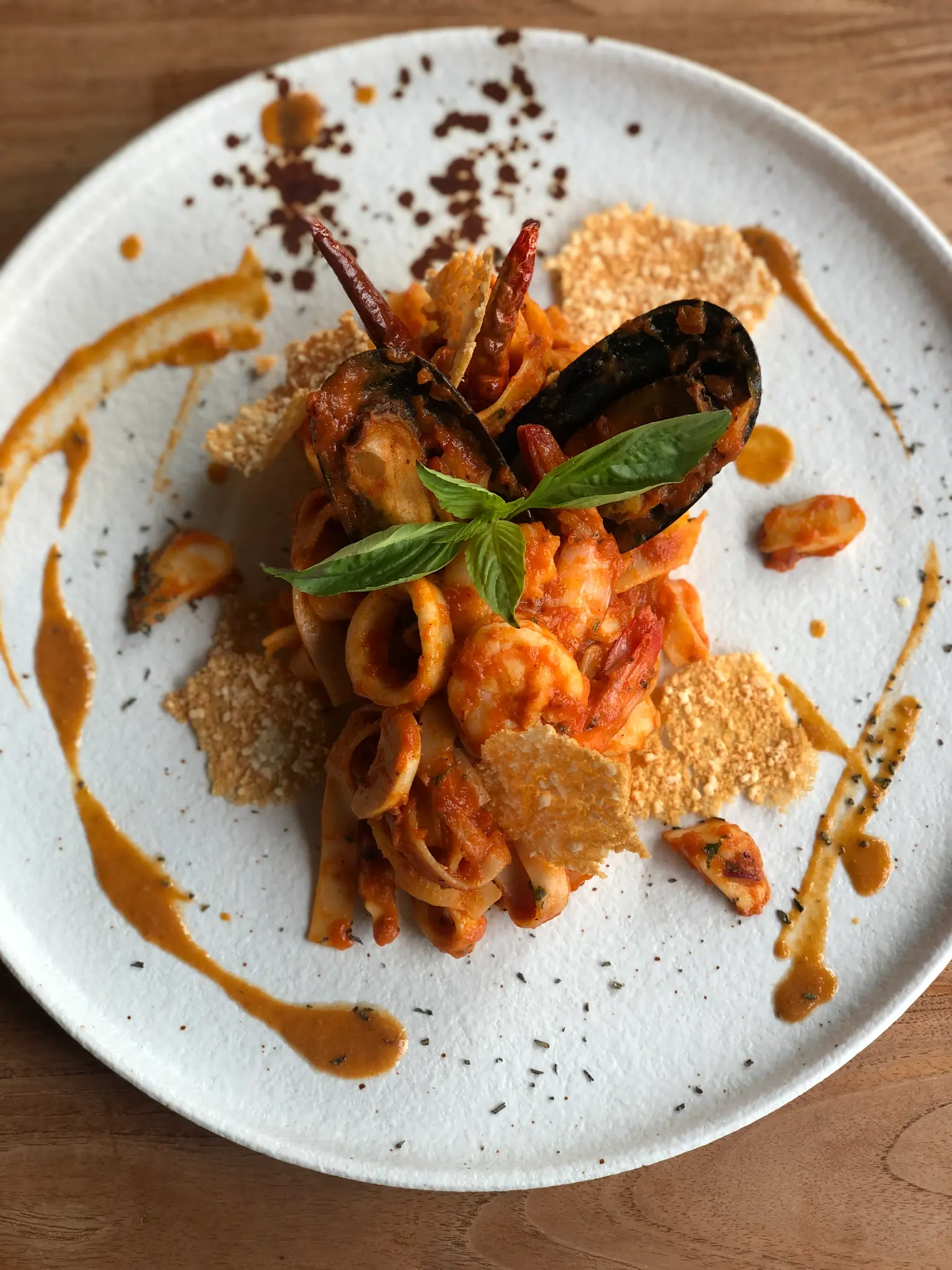 Seafood pasta on a white plate. Pasta, seafood, tomatoes and herbs are arranged with a considered finishing sauce.