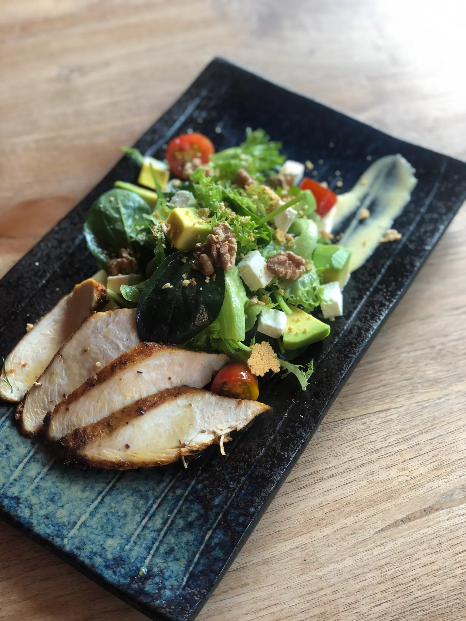 Sliced protein and garden greens. Sliced protein, garden greens and bright vegetables are arranged on a dark serving plate.