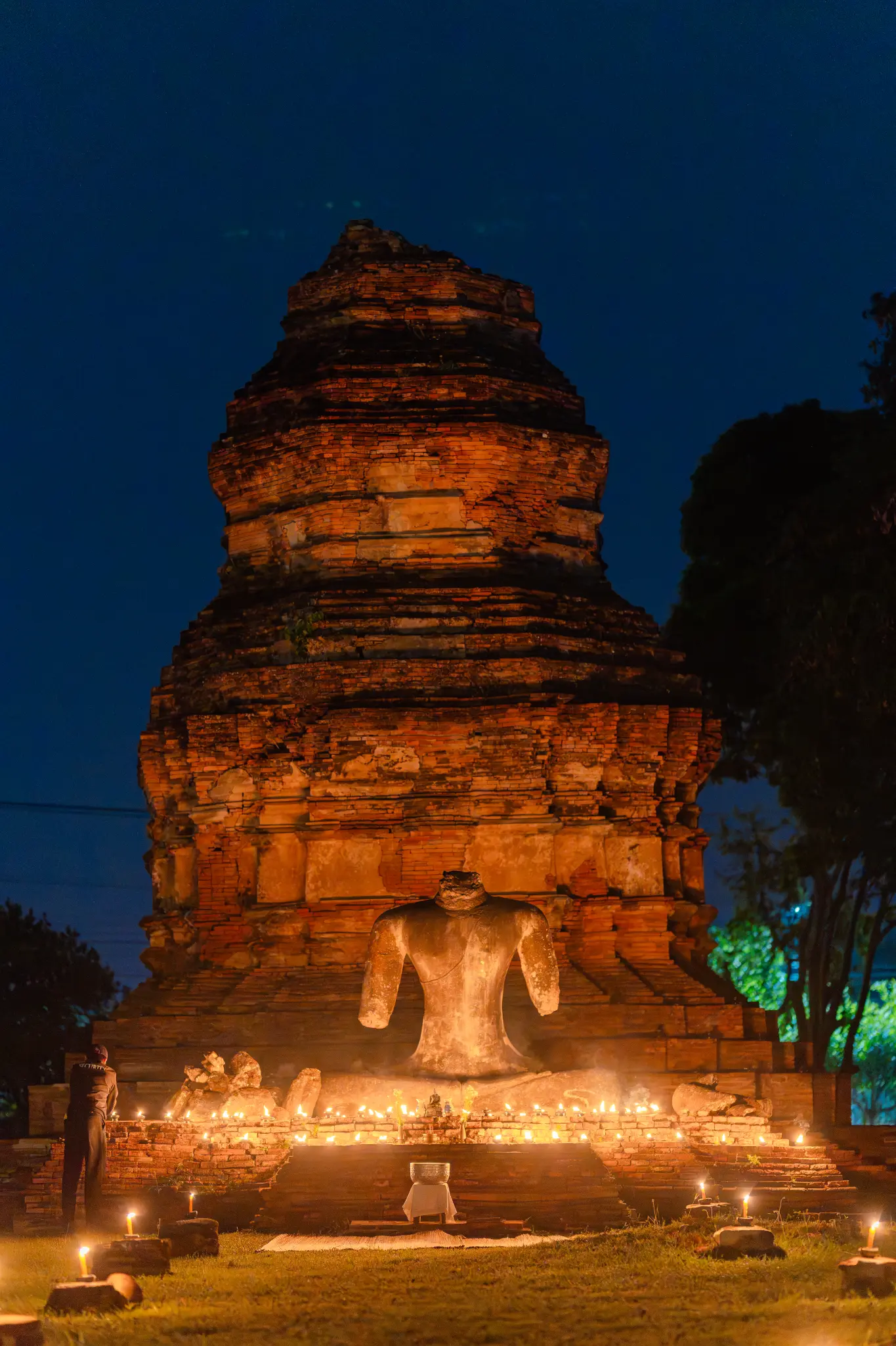 An ancient brick stupa and headless statue illuminated by candles at night