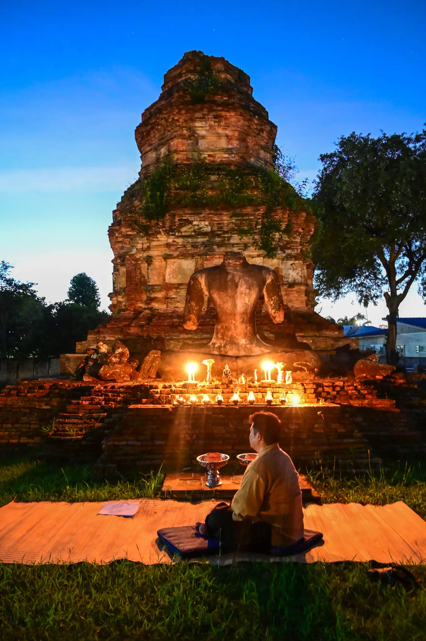A person meditating before an ancient brick stupa surrounded by candlelight at night