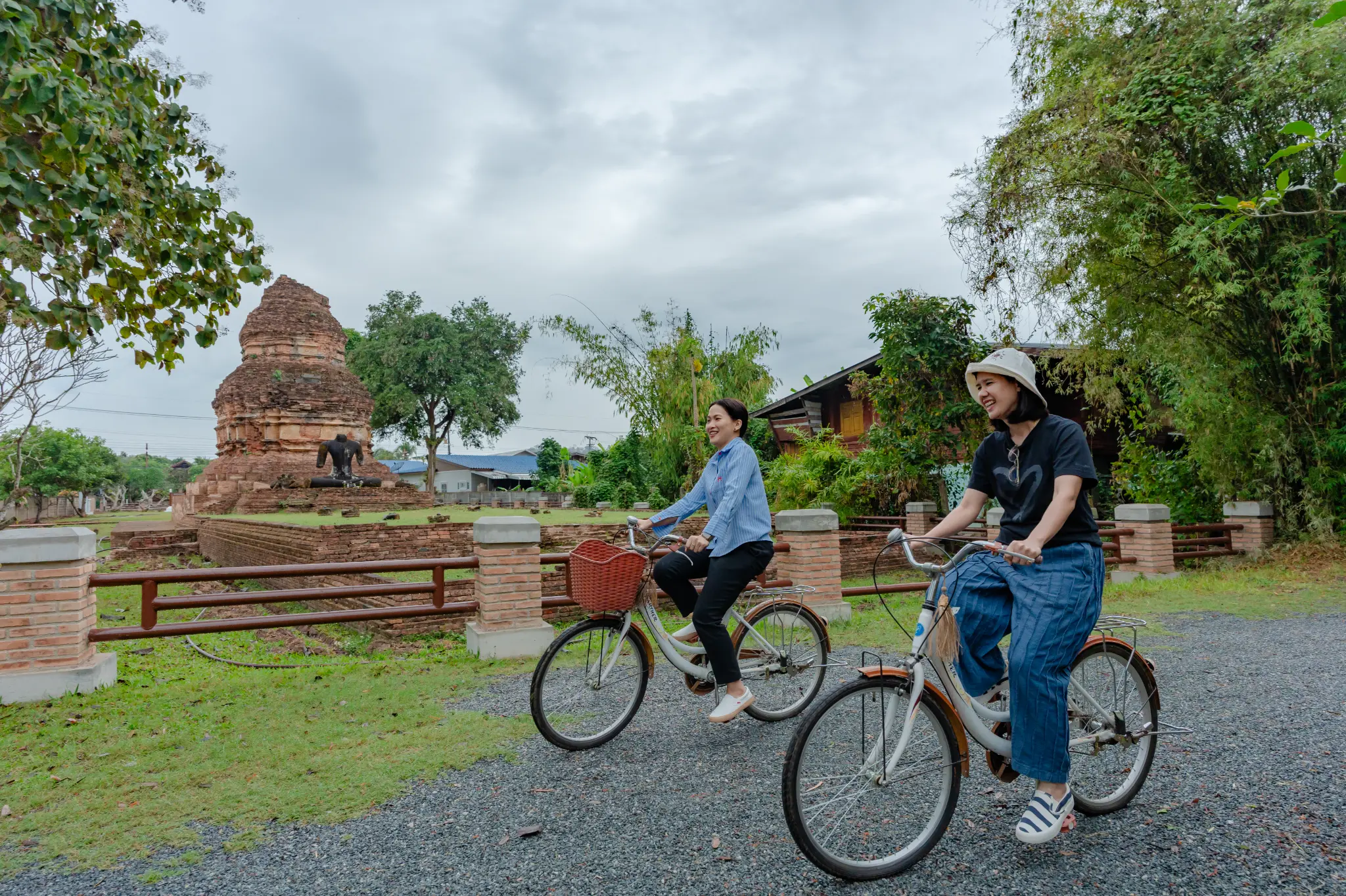 Two women cycling on a quiet road past ancient ruins and trees