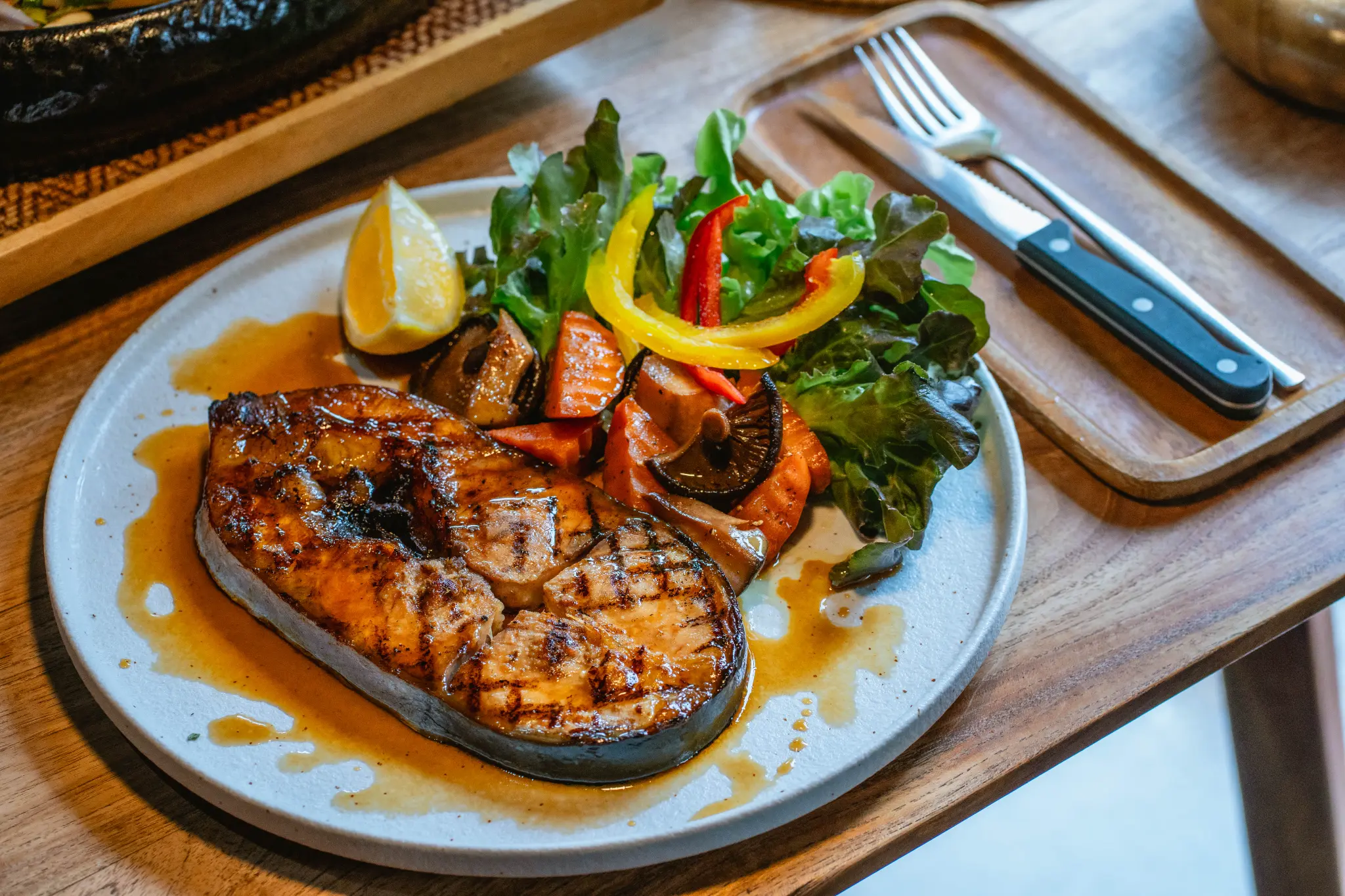 Grilled fish with mixed greens. A grilled fish steak is plated with mixed greens, bell peppers, mushrooms and lemon. Photographed at Wiang Neua Café & Restaurant in Chiang Saen, Chiang Rai.
