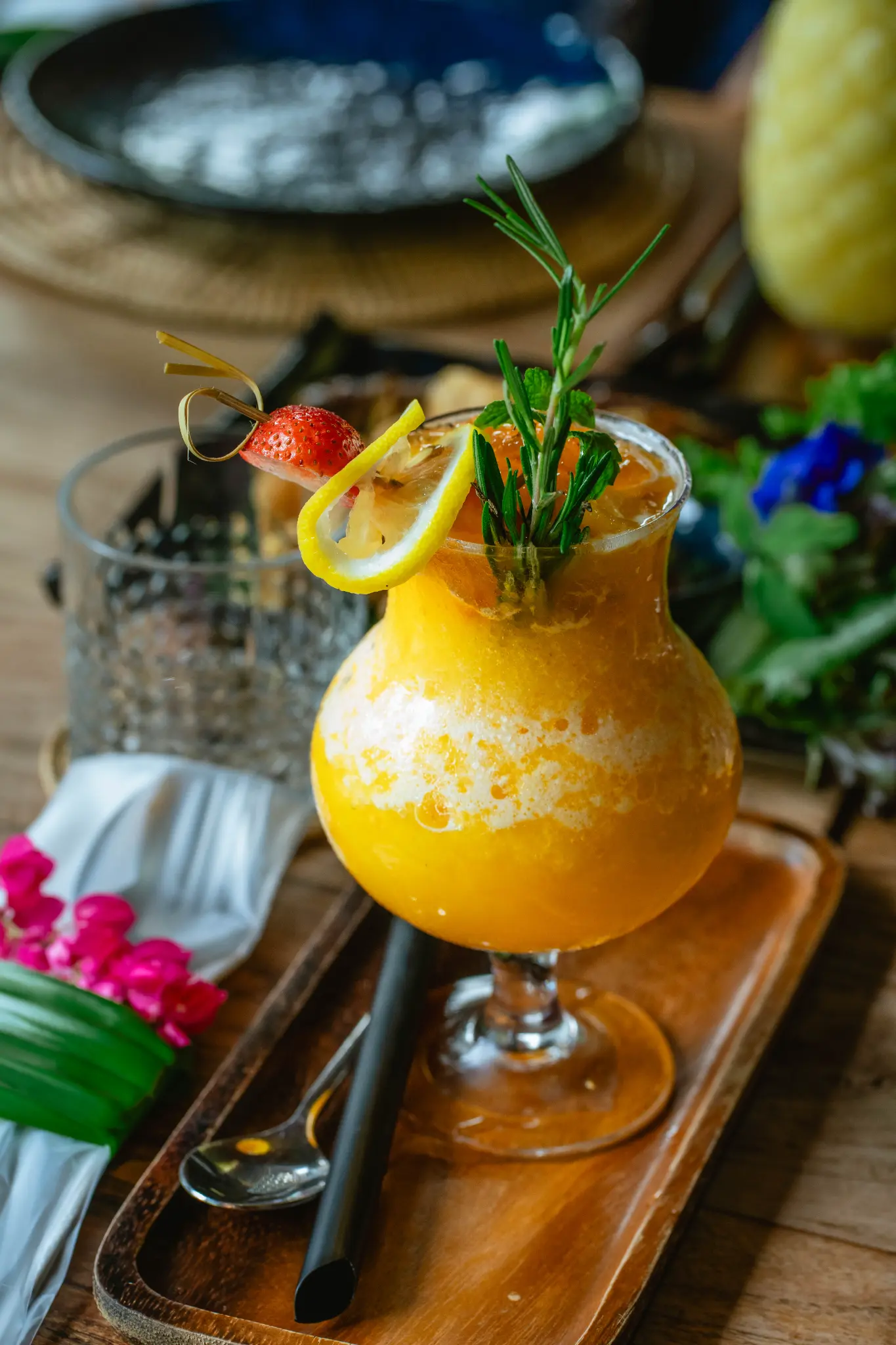 Yellow drink with fruit and herbs. A yellow drink garnished with strawberry, lemon, rosemary and mint is served on a wooden tray. Photographed at Wiang Neua Café & Restaurant in Chiang Saen, Chiang Rai.