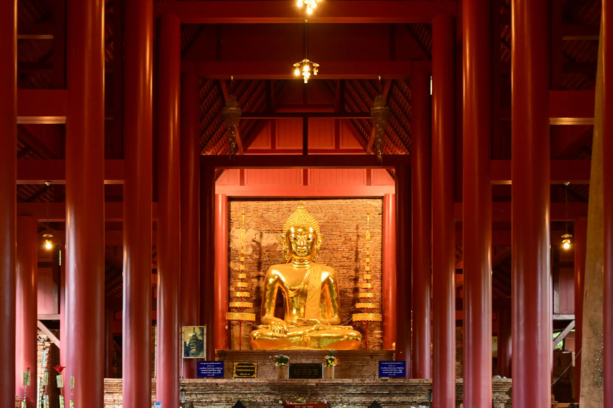 A golden Buddha image inside a symmetrical red wooden hall