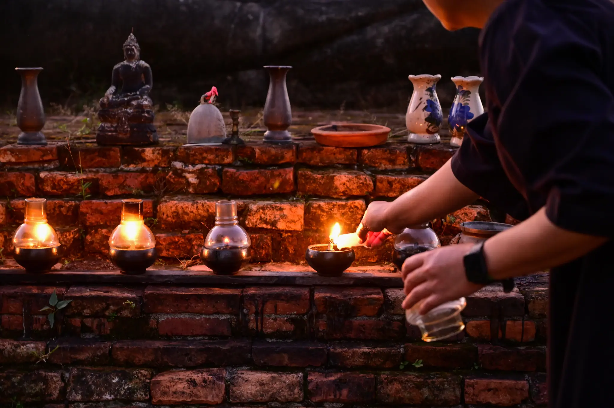A person lighting a lamp on a brick altar with a Buddha image and vases