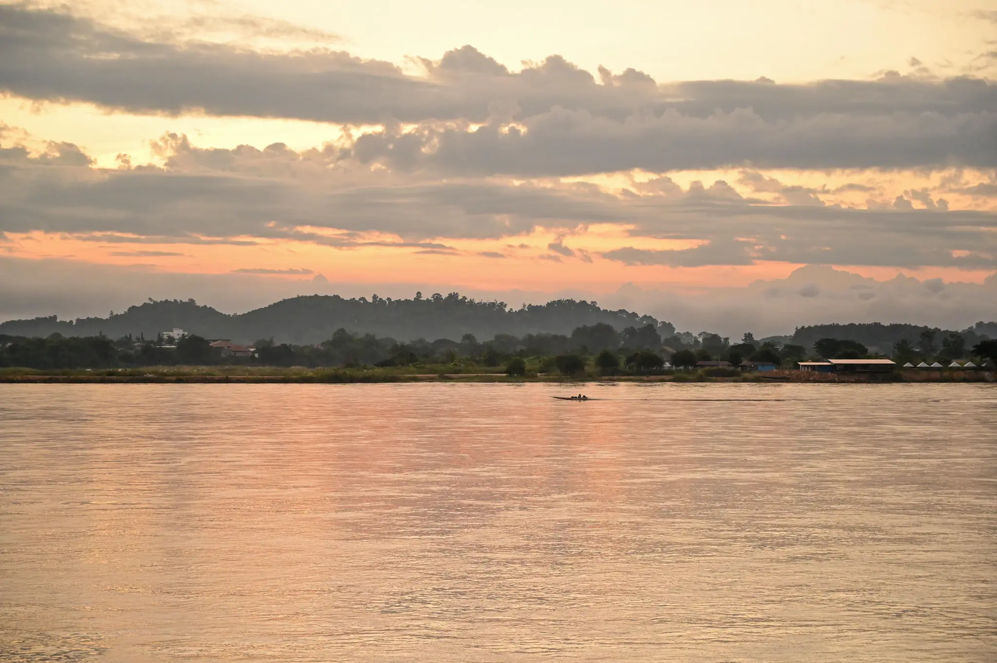 Sunset over the Mekong with a small boat and distant hills