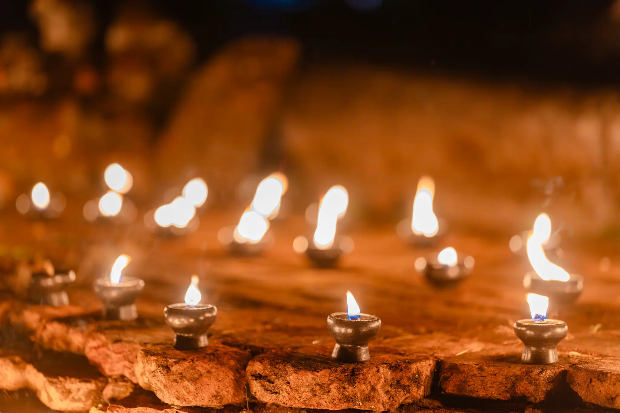 Small oil lamps glowing on a rough stone surface at night